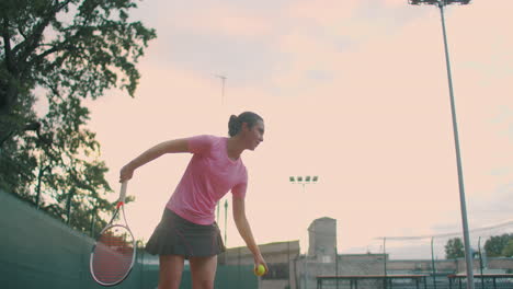 Slow-motion:-female-sportsman-during-her-practice.-A-close-up-of-a-girl-athlete-serves-the-tennis-ball.-Young-woman-is-hitting-the-ball-with-her-tennis-racket-at-sunset